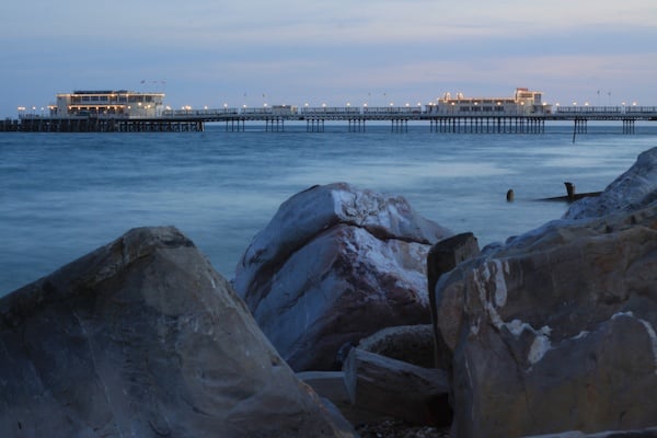 22 4s landscape photography of a pier with rocks in the foreground and boats in the background