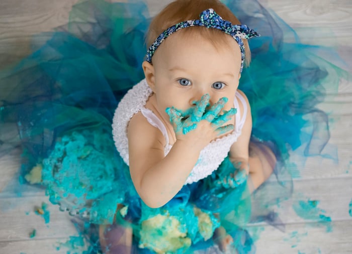 Cute portrait of a baby eating a green cake and looking up at the camera - DIY Cake Smash Photography