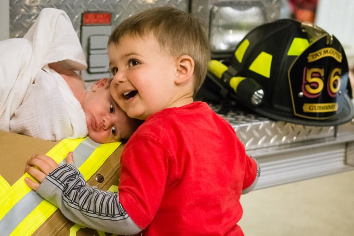 A family portrait shot of a little boy and newborn baby posed with fireman paraphernalia