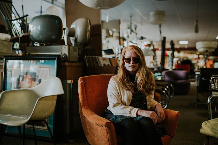Self-portrait of a woman sitting in an armchair in a thrift shop