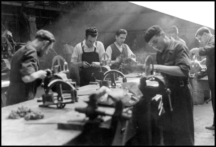 Black and white photo of men at work in a factory by Gerda Taro