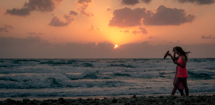 A couple walking on the beach at sunset.