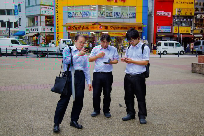 three men looking at their phones on the street