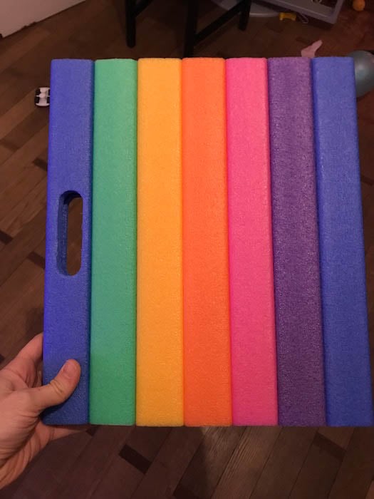 A vibrant, colorful foam board with a rainbow of colors and it is held up by a person. 