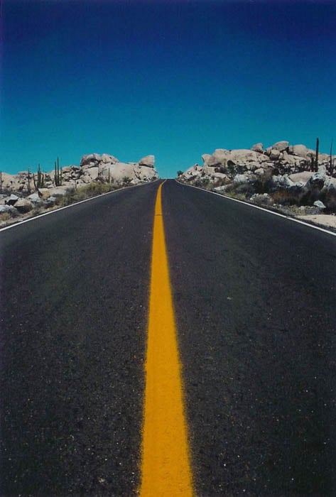 road photo of a highway leading into the horizon, blue sky and yellow striped road