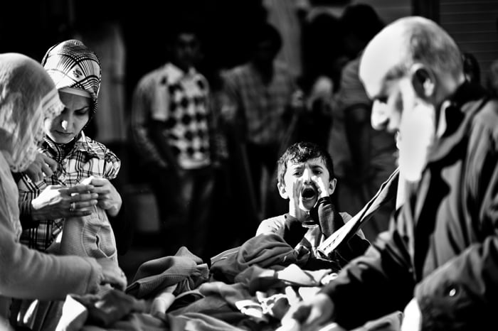 Black and white travel photo of a market in Istanbul, a young boys shouts towards the camera while adults look through fabrics