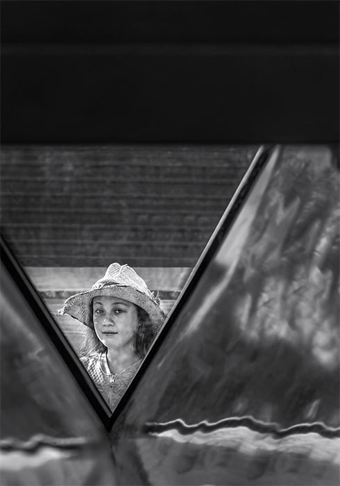 Black and white photo of a girl in white hat framed by architectural detail. Creative street photography