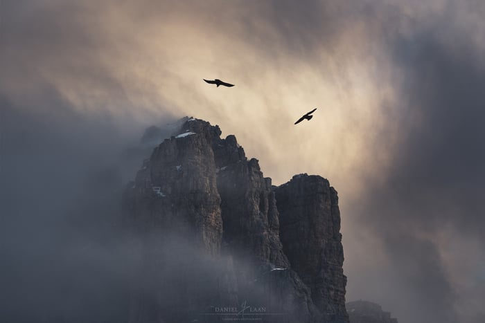 An eerie and dramatic fine art landscape photography shot of a rocky mountain being circled by birds and a stormy overcast sky.
