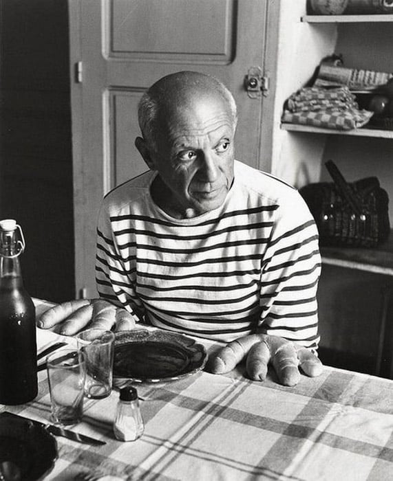 Robert Doisneau black and white photograph of Pablo Picasso sitting at a table posed as if bread were his hands