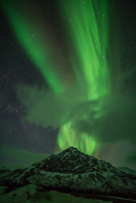 Photograph of the northern lights in Alaska with an icy mountain in the foreground