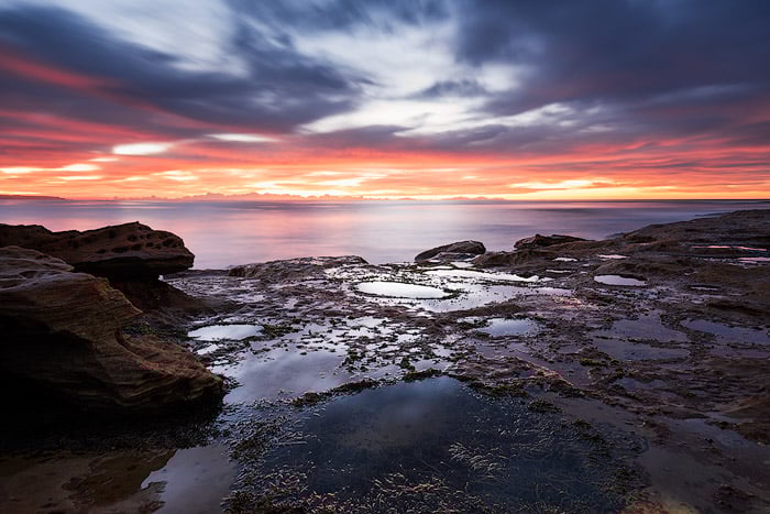 A dramatically lit rock pool seascape with fiery sunset.