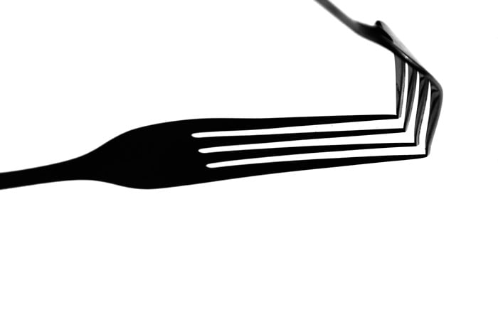 A black and white close up photograph of a fork with a strong shadow beneath.