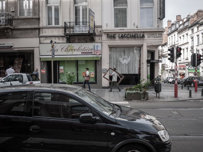 a busy urban street scene containing cars, people, shop fronts and buildings