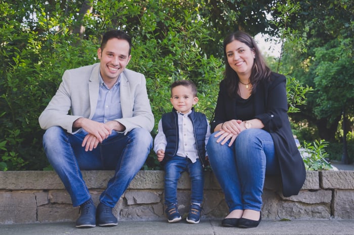 Family portrait photo of a couple and son sitting on a wall outdoors