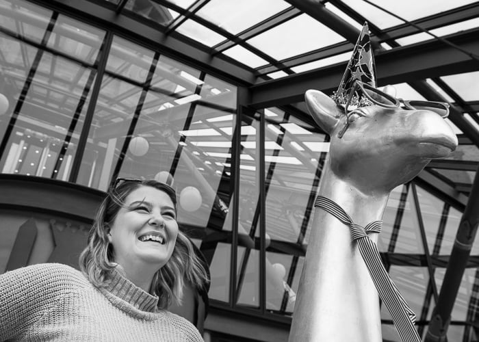 A black and white street photography shot of a woman beside a sculpture - black and white vs color