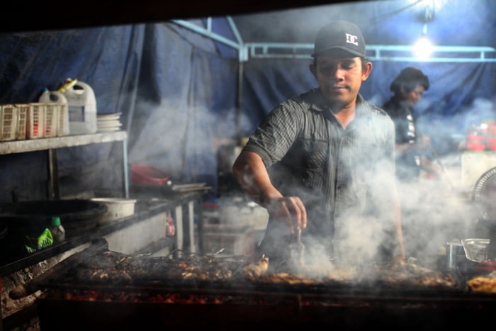 Street photography of a man cooking on a grill inside a tent- travel photography checklist.
