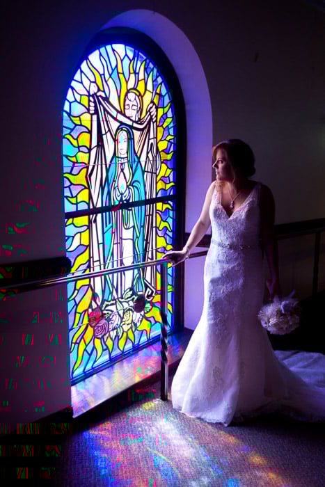 A photo of the bride posing by a large stained glass window - natural wedding photography lights