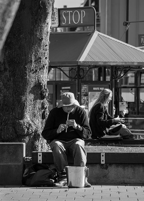 Black and white street portrait of a man playing a flute outdoors on a bright sunny day - street photography lighting
