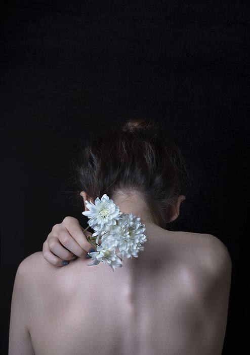 Artistic fine art portrait photography of the back of a female model holding white flowers towards the camera