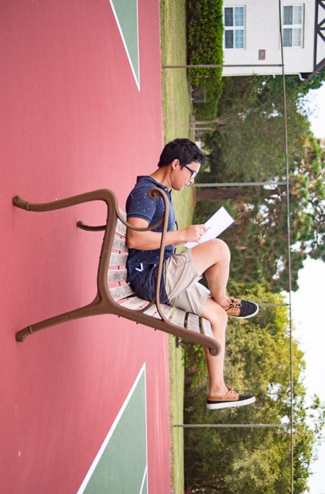 Humourous forced perspective photo of a man taken at angle which makes him look like he is sitting upside down on a bench reading a newspaper
