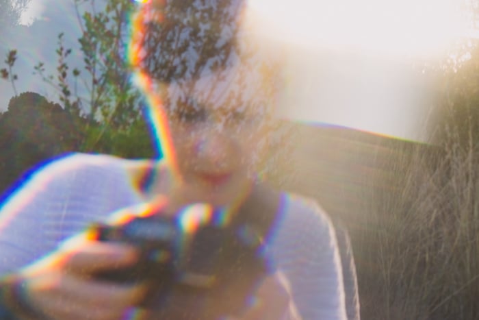 A woman in a stripy top holding a camera, overlayed with dreamy prism photo effect