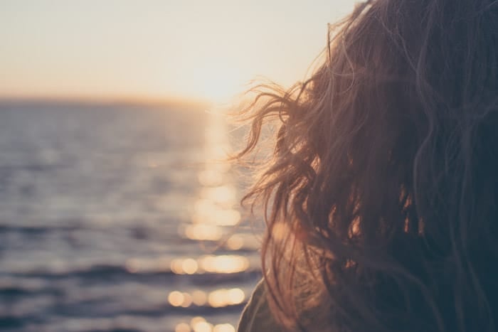 Dreamy portrait photo of a girl looking towards the sea at evening time