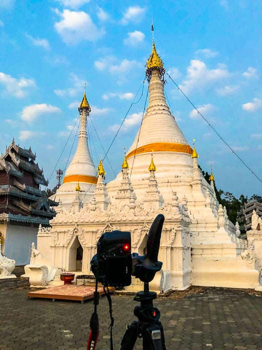 camera on tripod ready to photograph Bhuddist stupa against a bright blue sky in the early morning