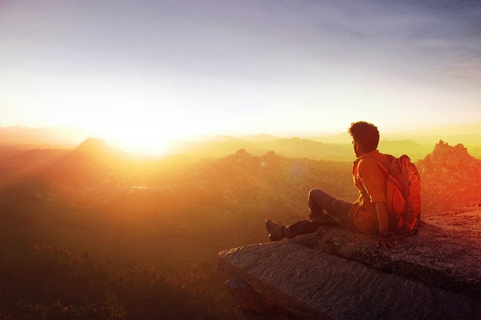 Man sitting looking out at mountains during sunset
