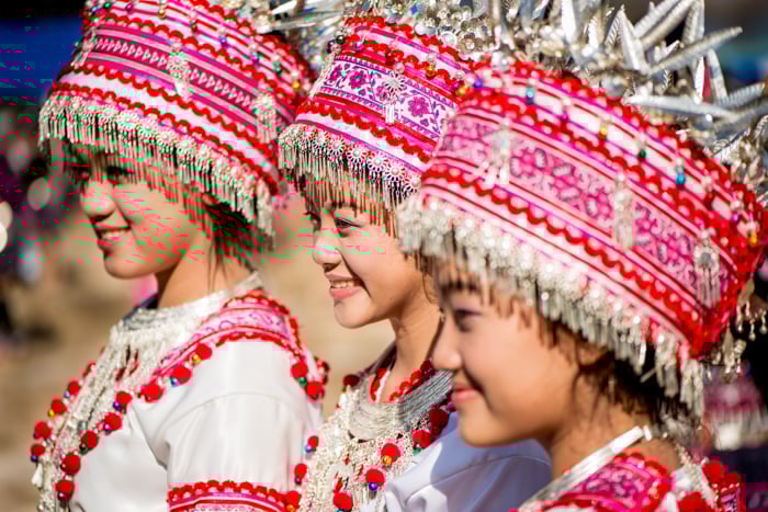 three smiling girls wearing red and white traditional headdresses and costumes
