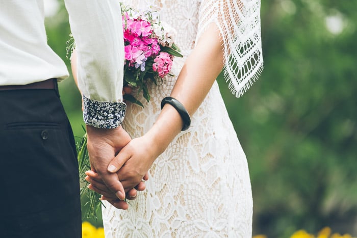 A closeup portrait of the bride and groom holding hands outdoors