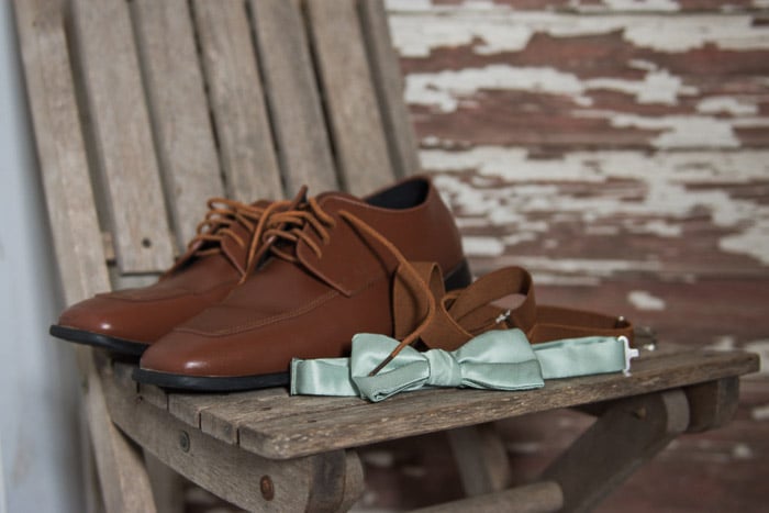A shot of a pair of wedding shoes and a bowtie on a wooden chair