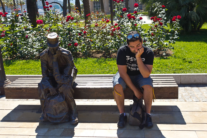 A man sitting beside a statue on a bench