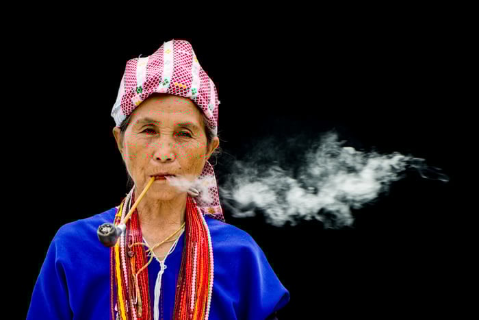A Karen Woman Smoking a pipe against a black background - figure to ground photography composition