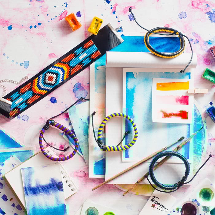 woven straps and bracelets on watercolor paintings on a pink and blue watercolor background