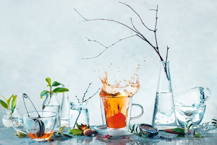 Tea cup with a dynamic splash and glass bottles with green plants and tree branches in a high-key spring still life. Cleanness and freshness concept
