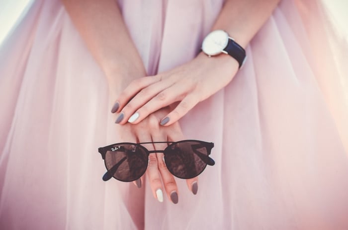close up of a model in a pink dress holding a pair of sunglasses
