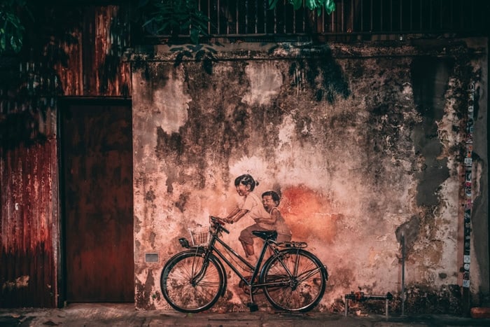 Atmospheric photo of a mural of two children on a bike on a stone wall in low light