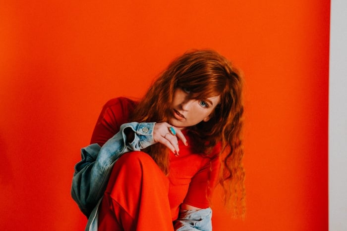 A red haired female model, wearing orange and posed in front of an orange background