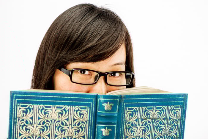 Asian woman with glasses on peering over a book