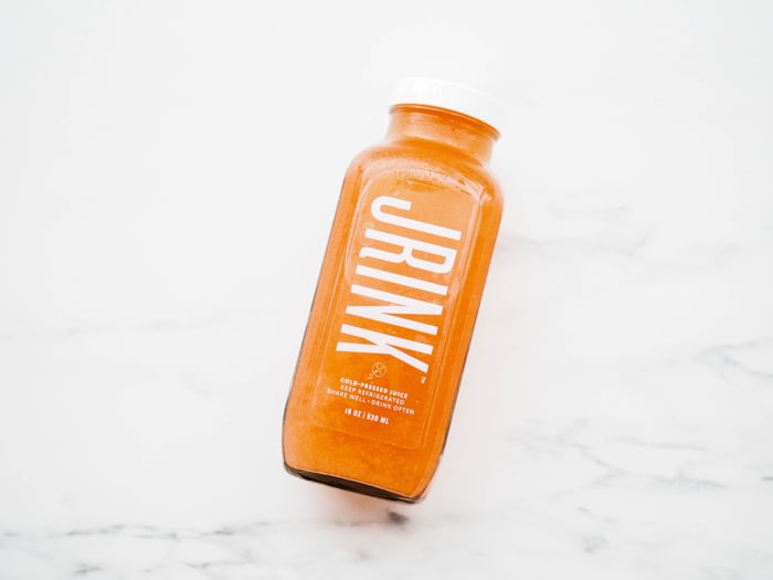 bottle of orange juice with name Jrink printed in white on the bottle, on a marble table