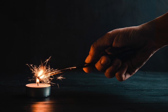 Sparkler photography: hand holding sparkler in a dark room, lighting the sparkler with a tealight candle