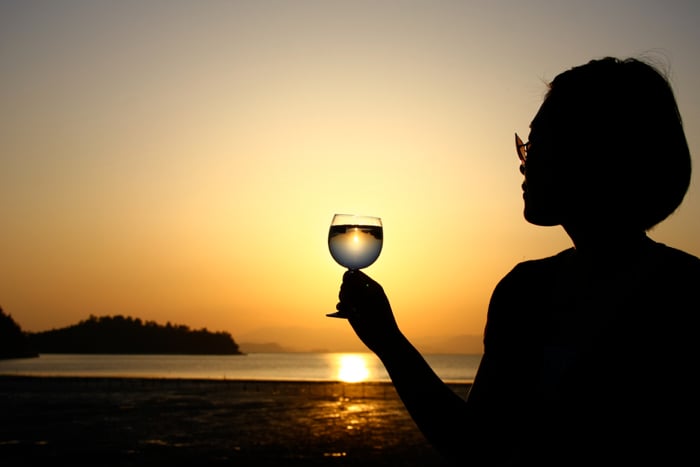 A silhouette of a female model against a beach sunset, holding a wine glass for the purpose of light refraction photography