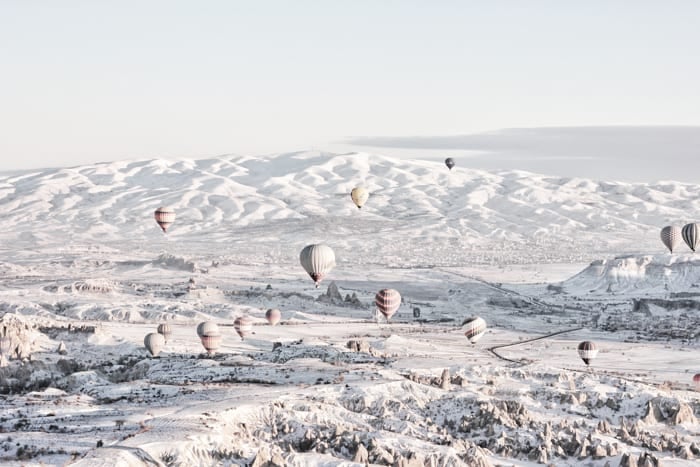 Many hot air balloons in flight over a snowy landscape