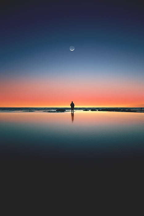 Stunning portrait of a lone figure on a beach below a colorful sunset - symmetry in photography