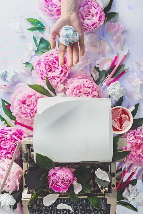A bright and airy flatlay of pink roses surrounding a typewriter 