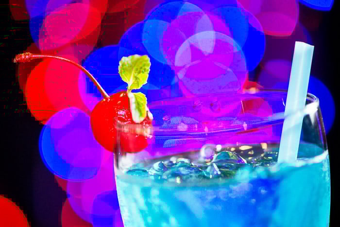 A close-up of a blue cocktail with blurry bokeh light background