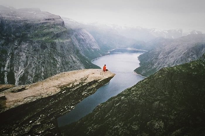 A candid photography example ofa person sitting on a cliff overlooking a stunning mountainous landscape 