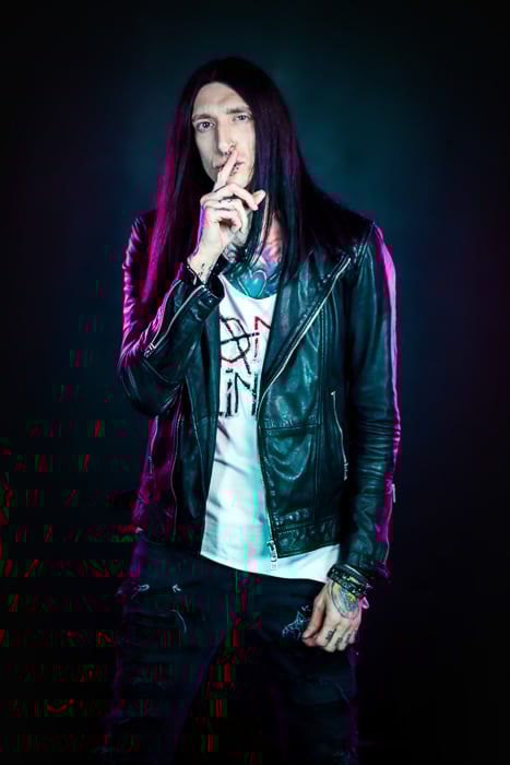 A portrait of a long haired male photography model posing against a dark background