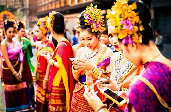 A street portrait of girls checking their smartphones before the start of the annual flower parade in Chiang Mai, Thailand. Photos that tell a story