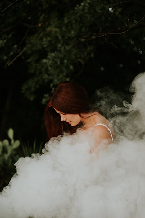 Dreamy portrait of a female model posing outdoors surrounded by smoke and dreamy background